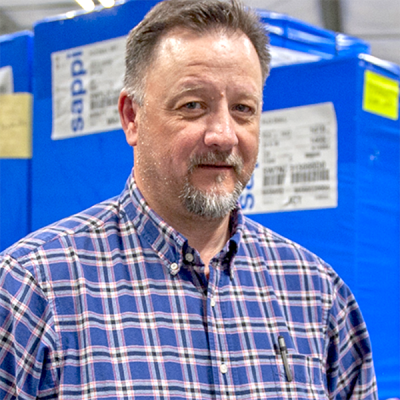 Portrait photo of production manager Randy Robertson in front of blue skids of paper.